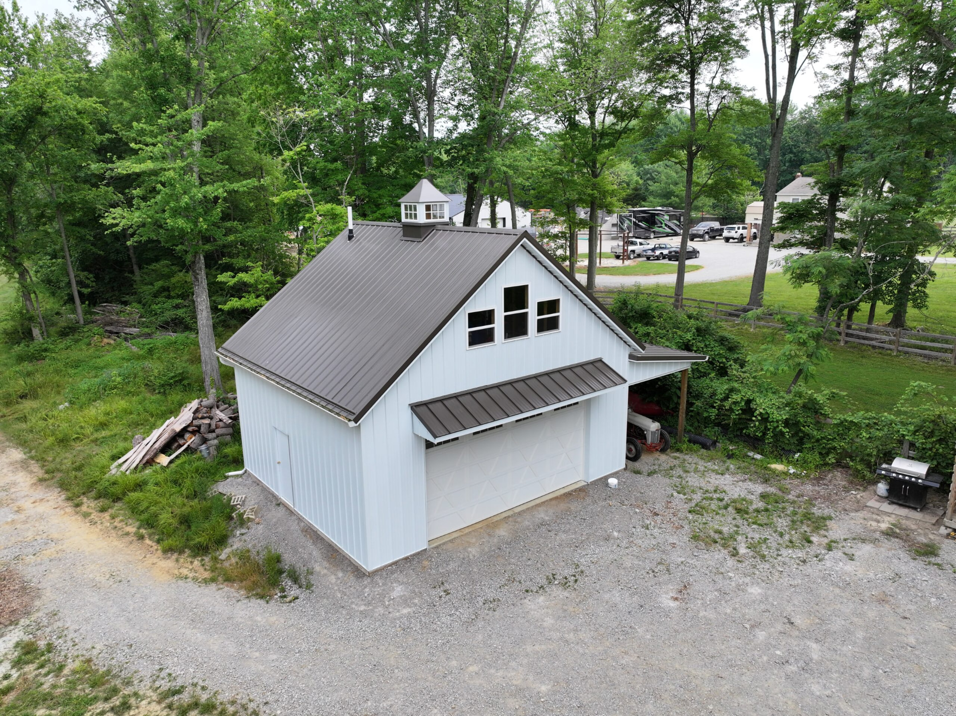 White post frame garage with cupola, gable overhang, and attached carport in wooded Southern Ohio
