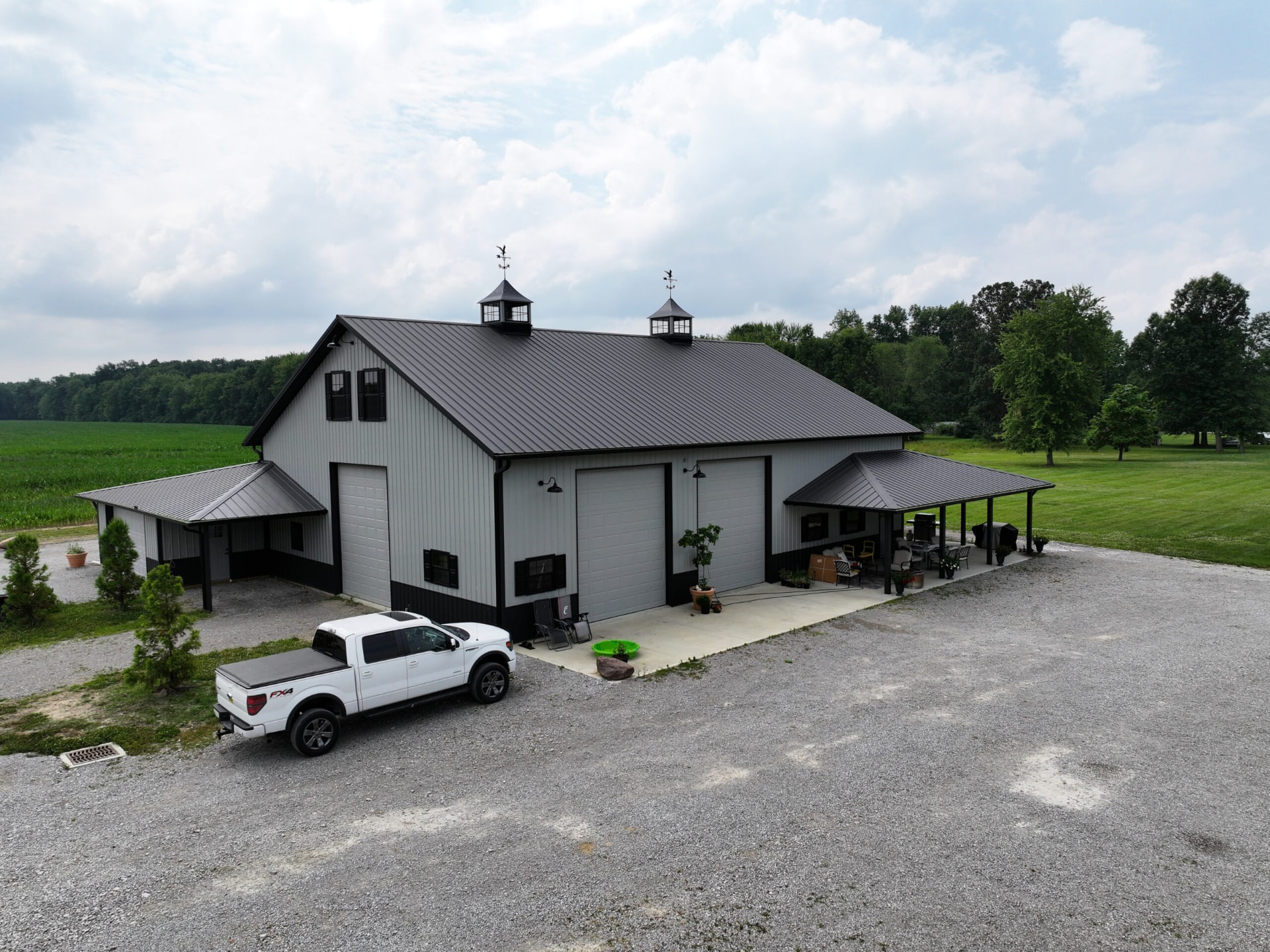 White post frame barn with dark metal roof, twin cupolas, and covered porch built by Graber's Construction in Adams County, Southern Ohio